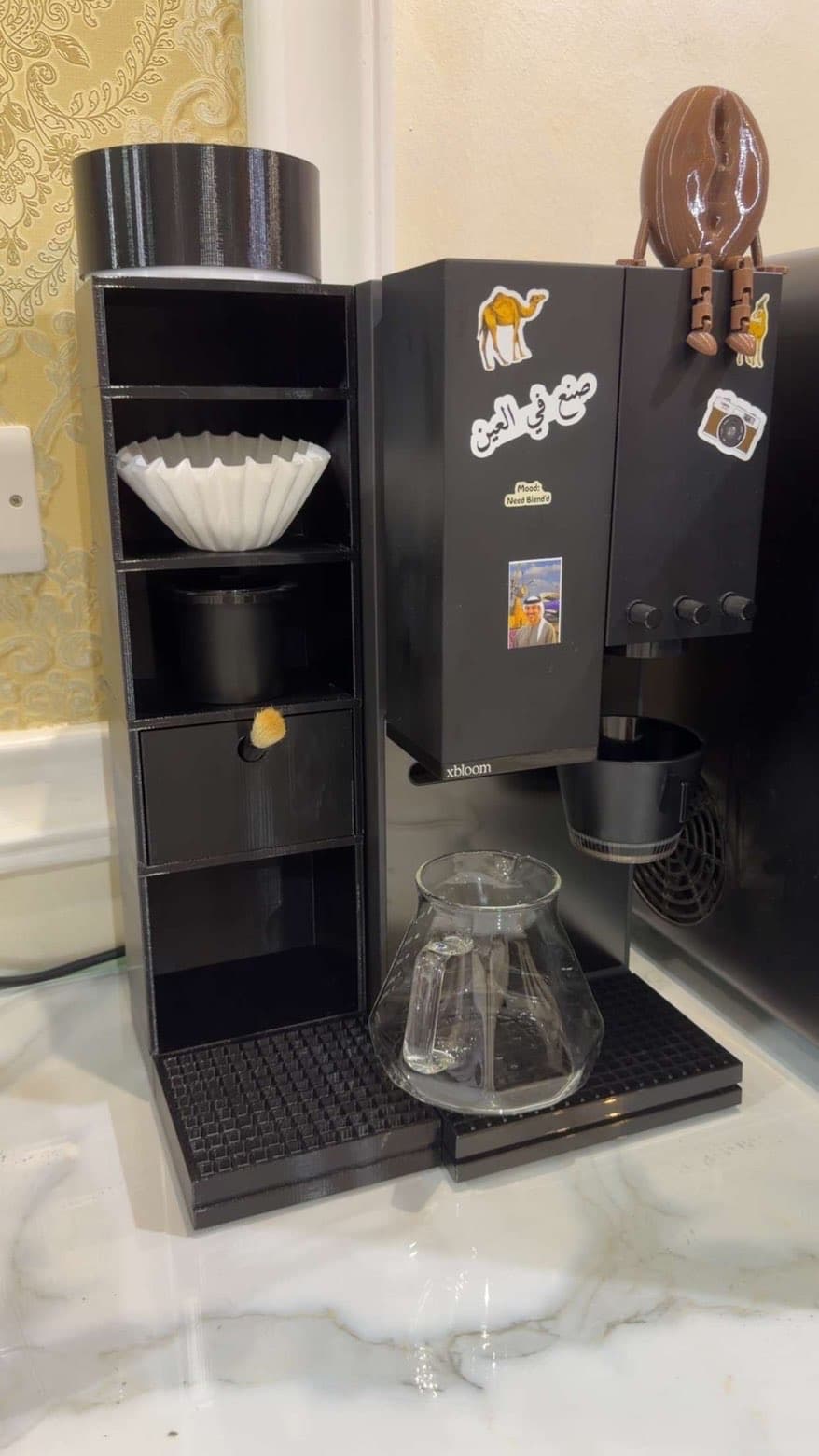 Compact printed coffee storage tower and filter organizer beside a coffee machine